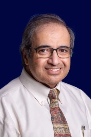 Portrait of a smiling elderly man with glasses and a patterned tie.