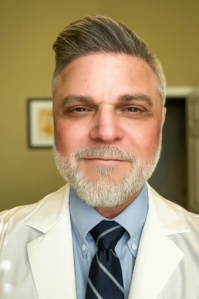 Smiling middle-aged man with gray beard in professional attire.