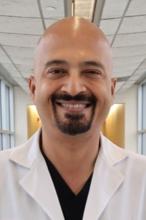 Smiling man in a white coat with a blurred background.